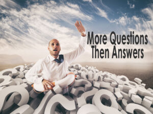 Man in a pile of pillows cut in the shape of question marks, raising hand looking for answers to question