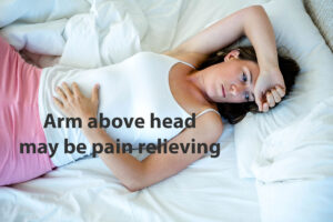 A female lying in bed with her arm above her head to ease shoulder pain