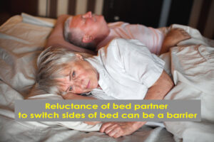 senior couple lying in bed, one awake, one asleep